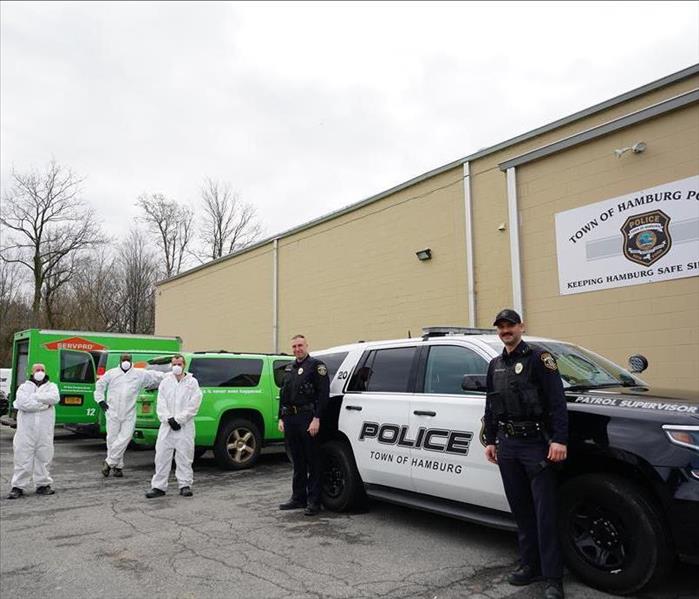 SERVPRO technicians in Tyvek posing with the Town of Hamburg police after sanitizing vehicles.