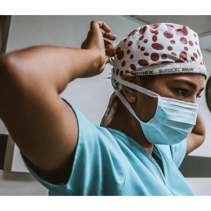 Doctor wearing head covering attaching a surgical mask.