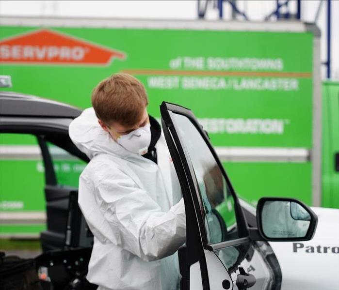 A SERVPRO technician in Tyvek cleaning the window of a police vehicle.